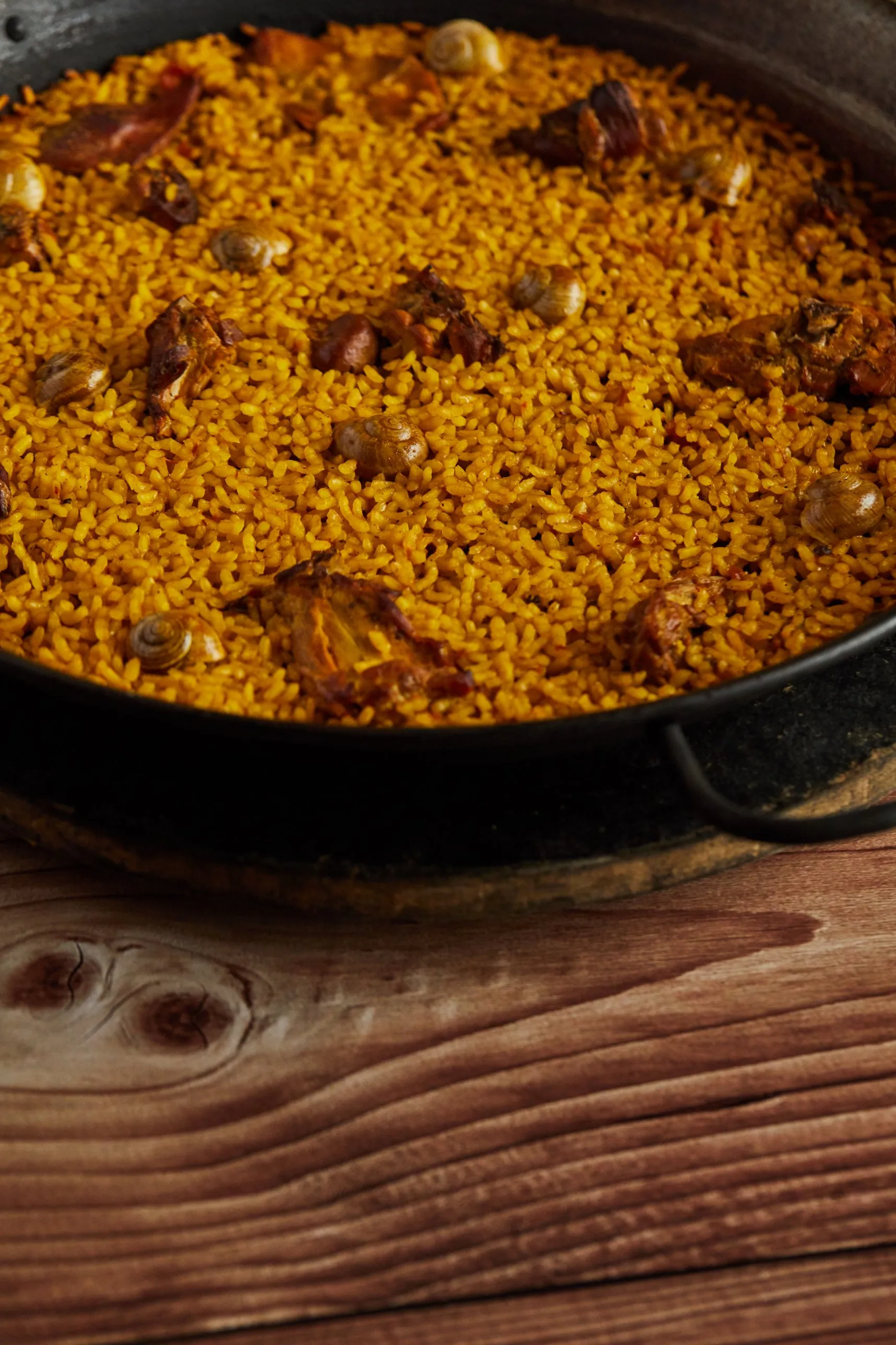 Arroz de conejo y caracoles en paellera de hierro sobre mesa de madera