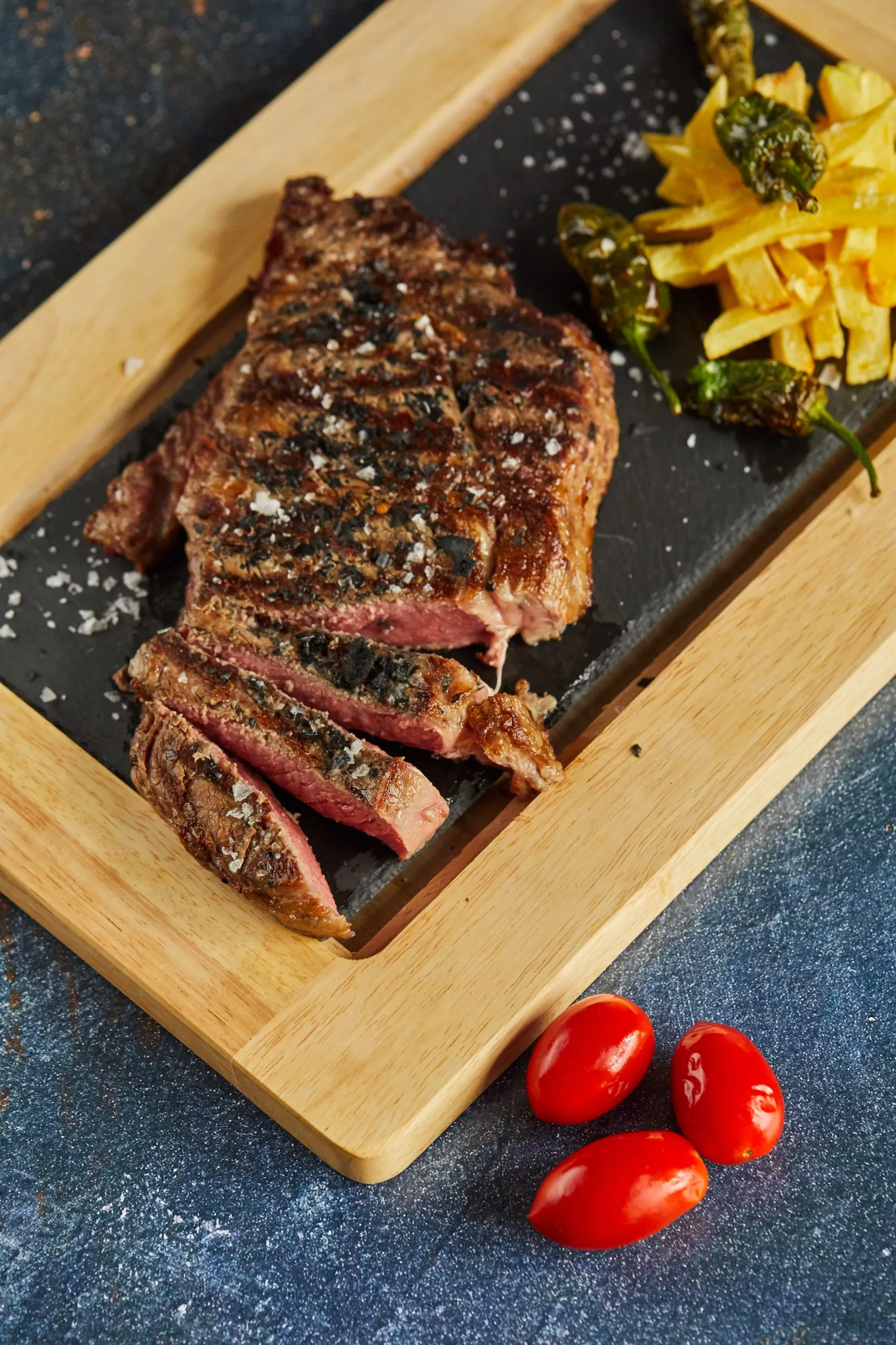 Carne a la brasa cortada al punto sobre pizarra, con patatas y pimientos de Padrón