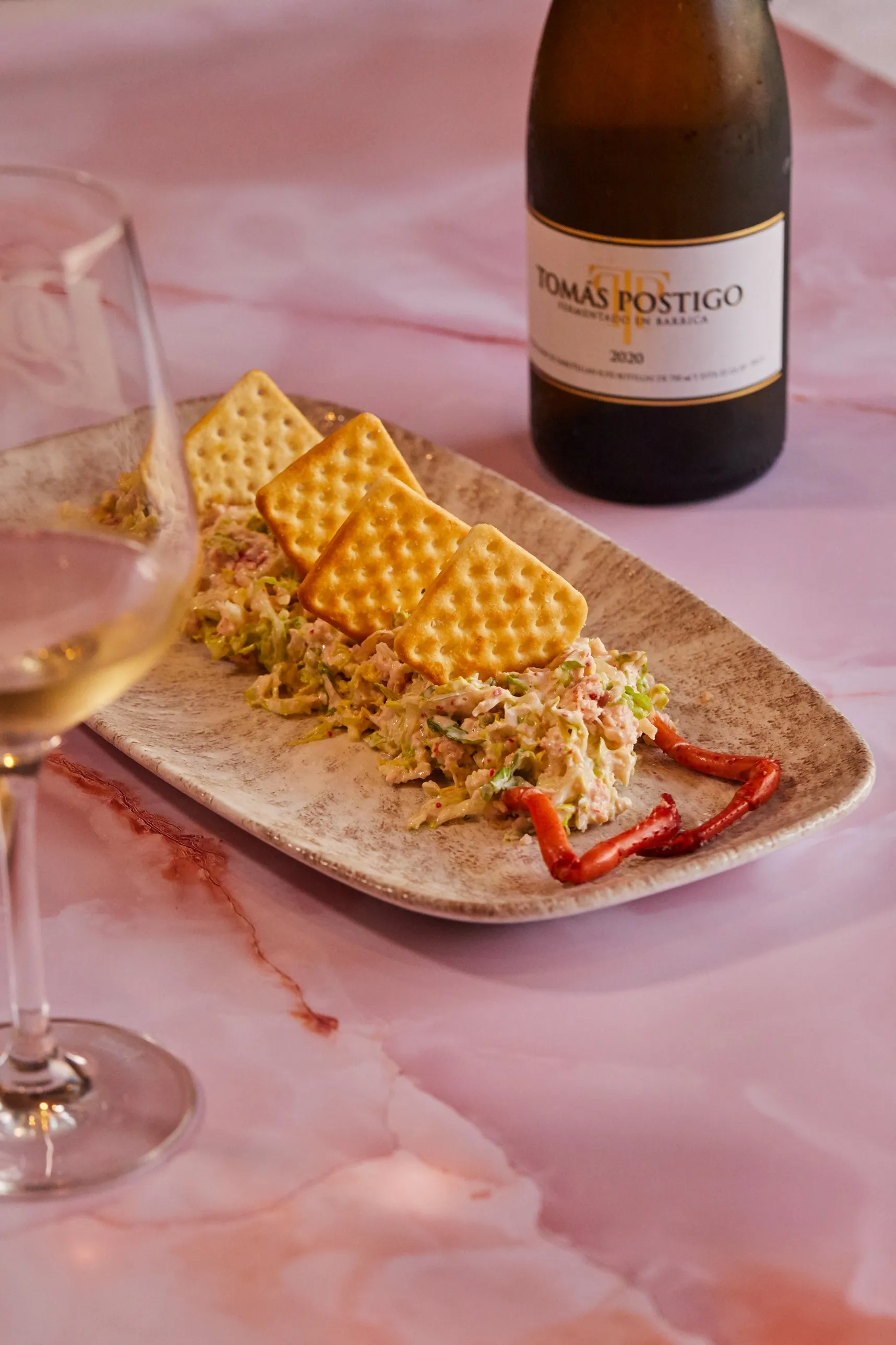 Ensaladilla de bogavante con galletas saladas, una copa y una botella de vino blanco
