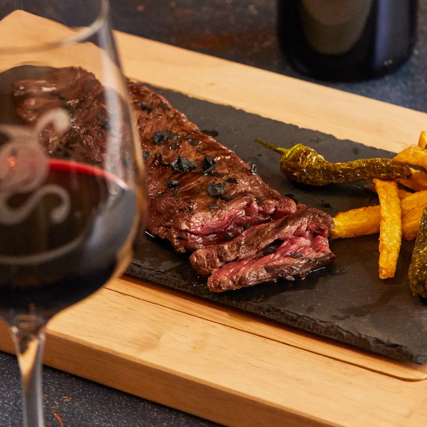 Entraña de wagyu a la brasa sobre pizarra con pimientos y patatas