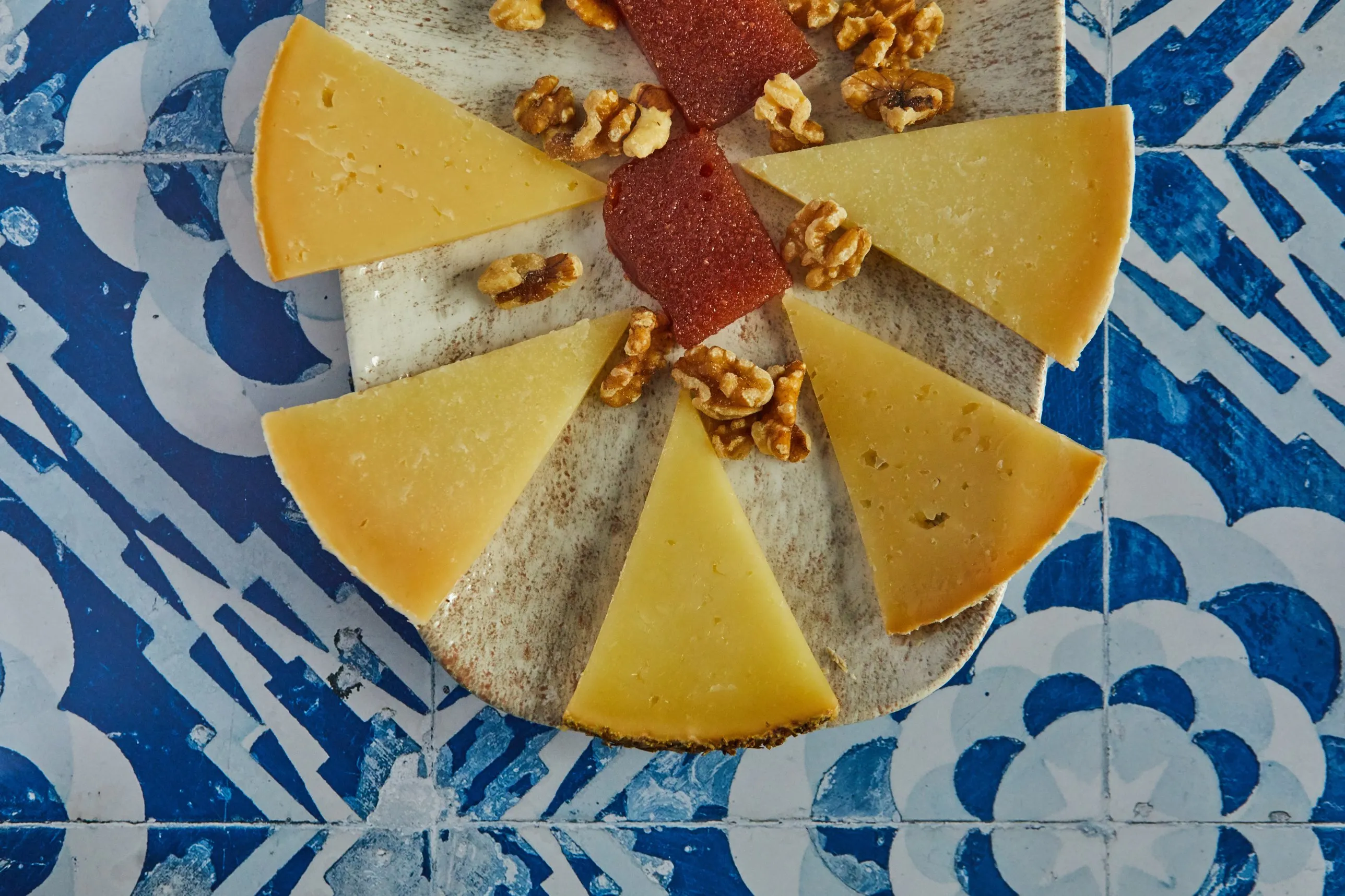Tabla de quesos con membrillo y nueces sobre mesa de azulejo